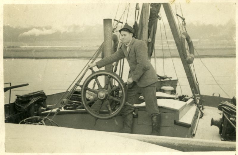  John Leather at the wheel of a barge. The location 
is Rowhedge Ironworks where John worked as a draughtsman and surveyor as 
evident by the leather patches on his elbows. It is probable that work 
is being done on the rudder as sheerlegs can be seen with the take'll coming down near the main horse. A steam train has just left Wivenhoe and 
heading towards Colchester and there appears to be a ...
Cat1 [Not Set] Cat2 Barges-->Pictures Cat3 Places-->Rowhedge