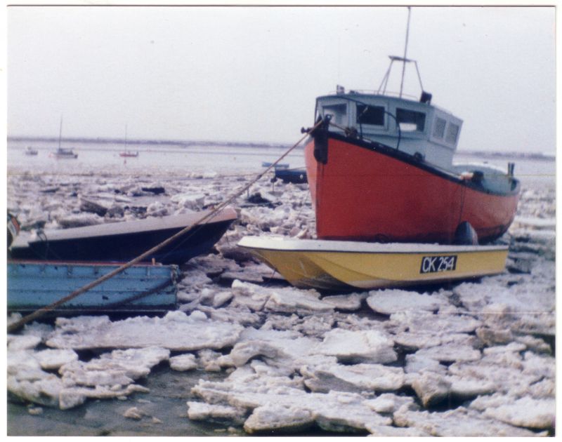  Boats at West Mersea in an icy winter. 

Terry Kyle says:

The yellow dory in the foreground was Chris Stopford's, and then later owned by Graham Rampling. The dory is fibreglass and has a modern 2 stroke outboard on it. The photo was probably taken in the late 1980's as I remember one hard winter thereabouts when fishing boats came out of the ice to lay on the edges, This looks like punt ...
Cat1 Weather Cat2 Mersea-->Creeks, fleets, channels, saltings
