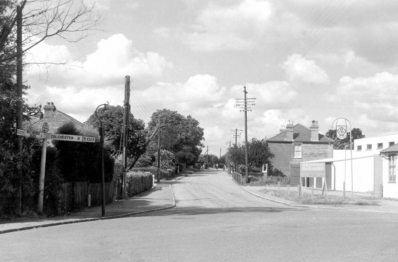  High Street North from corner of Barfield Road. B1025 finger post on the left. Griffon Garage on the right, probably Griffon Garage to the right probably owned by Norman Thorpe and Mr Bishop at this time.

The B1025 finger post is now in Mersea Museum. 
Cat1 Mersea-->Road Scenes Cat2 Mersea-->Shops & Businesses
