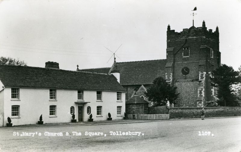  St. Mary's Church and The Square, Tollesbury. The village lock-up is nestling by the church wall. Postcard 1109 mailed 30 October 1961.. 
Cat1 Tollesbury-->Road Scenes