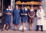 Repton Dixon's Stores in Church Road, West Mersea. All the shop staff.
1. Bessie Dixon (with her tongue out), 2. Pat Franklin, 3. Susan Hales, 4. Carol Dixon, 5. Percy Bacon.
<b>Pat Franklin</b> and her husband Gil (Gilbert) Franklin lived in Kingsland House in Kingsland Road which used to be a school. It was such a huge house and the upkeep was mind blowing. In the end they sold it up on condition it was kept intact as it was such a wonderful old house. Their wishes were not upheld and it was levelled and re-developed very soon after. 
<b>Susan Hales</b> she married Danny Williamson in 1967, He used to ride huge motor-bikes. Susan was a lovely bubbly girl.
<b>Carol Dixon</b> - little old me in the brown overall and then my beloved Percy Bacon, my we had some fun in those days but we worked hard and the days were long.
In the evening after the shop shut at 6pm we had a meal and then I had to cash up all the tills, agree them and put the float back for the next day. Then all the duplicate invoices had to be entered into the ledger for every sale that day 'on-tick' which would be put on the customers monthly accounts at the end of every month. All this was done by hand entry, no machines in those days and the till roll was folded into lengths of about 10 inches and each section added up using mental arithmetic. In the summer days when holiday makers were down the till roll could easily be 10 to 15 foot long and if the cash did not agreee with the pencilled entries on the till roll it was a long night! The off-licence had a separate till and ledger so I was rarely finished before 8pm and we opened at 8am.
Part of CW3_105. c1965. Photo: Carol Wyatt