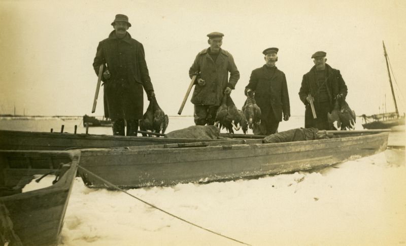  Gunners & punts. Winter weather. BJ: About 1930 Local wildfowlers, left. to right, Tom D'Wit, Navvy Mussett, Clarke Mussett and Bill Mussett retum with a good bag of black geese. In the foreground are two good examples of local Mersea Punts complete with Punt Guns. 
Cat1 People-->Fishermen and Seamen Cat2 Wildfowling Cat3 Families-->Mussett