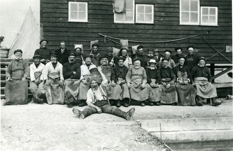  Tollesbury and Mersea Oyster Company men outside the Packing Shed circa 1908. Zeb Milgate (John Milgate's grandfather and Heather Haward's great grandfather) in foreground with basket. John Hewes in back row with white smock and highest shovel. William Haward (Richard Haward's grandfather) sitting in front row, third from right 

Back row (left to right) John Pierce, J. Maskell, Joe Pierce, ...
Cat1 Mersea-->Packing Shed Cat2 Fishing Cat3 Oysters-->Pictures Cat4 People-->Fishermen and Seamen