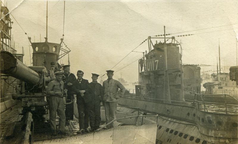  Royal Navy seamen aboard a submarine. To the right are submarines U117, UB148 and AK1.
Photograph thought to be taken at Harwich between November 1918 and May 1919.

U117 in WW1 was a long range minelayer submarine. After the war, she was surrendered at Harwich about 21 November 1918. In March 1919 an American crew took over and sailed her to USA. She was sunk as a target in 1921. ...
Cat1 Ships and Boats-->Naval Cat2 Places-->Harwich Cat3 War-->World War 1