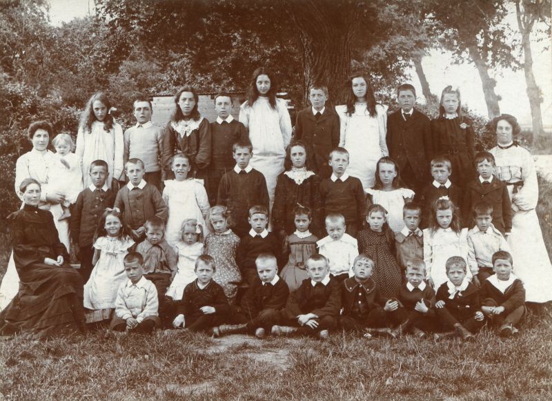  East Mersea School c1906. The headmistress Alice Mary Harvey née Pullen is seated on the left and her daughter Kathleen Grace is being held by the lady (a governess ?) standing behind her.

Photograph by A. Bond, Photographer, 92 Heath Road, Norwich. 
Cat1 Mersea-->Schools-->Pictures Cat2 Mersea-->East Cat3 People-->School