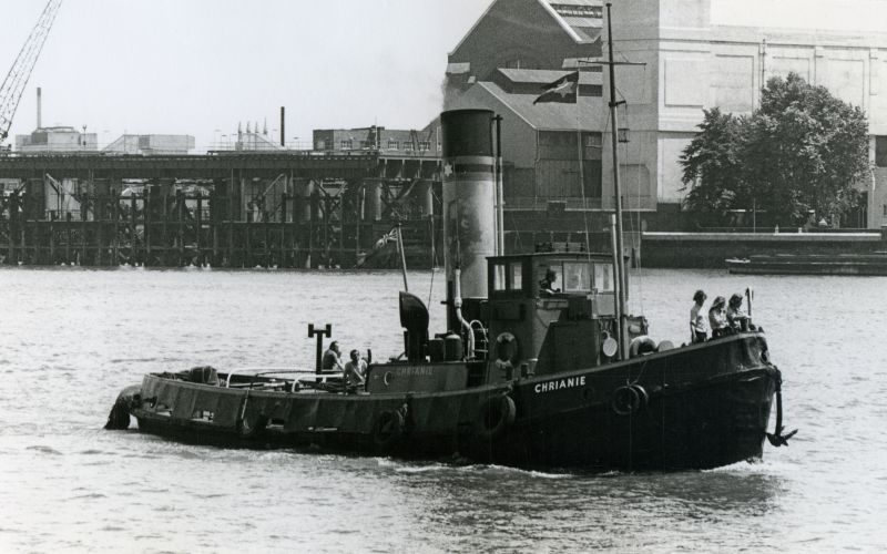  Steam tug CHRIANIE on the River Thames. Barry Pearce in the wheelhouse [ Janet Hall ].

From Tug Album 2, loaned by SSBR via Don Wright. 
Cat1 Ships and Boats-->Tugs Cat2 Places-->Thames