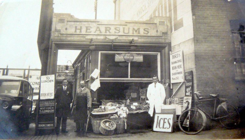  Hearsum's shop at the side of the St Johns Street bus park in Colchester. This is on the west side of the bus park.

L-R a busman, Robert Hearsum - Bob's father with black apron, and Bob Hearsum in white. 
Cat1 Mersea-->Shops & Businesses