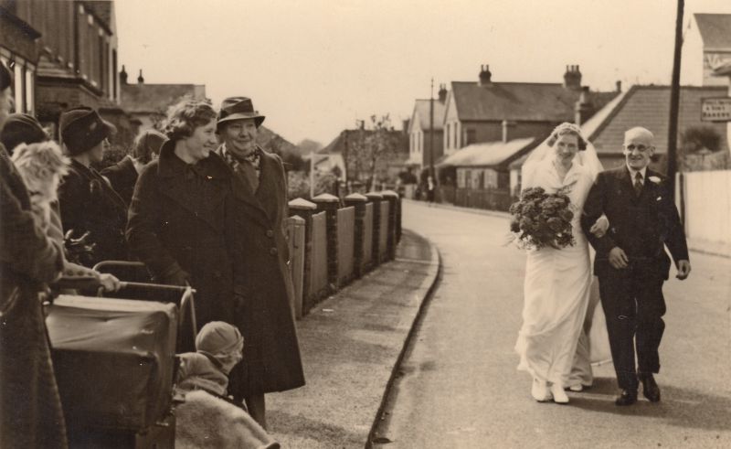  Florence Smith with Fred G. Smith walking to her wedding in Top Chapel. Mill Road. Mrs Laddie Hewes with hat on path. [RG] 
Cat1 Families-->Smith Cat2 Mersea-->Road Scenes Cat3 Families-->Hewes