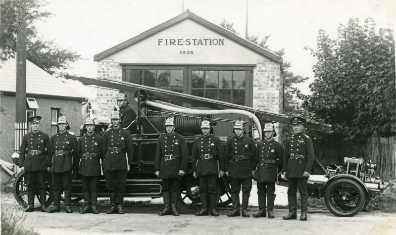  Fire Brigade c1938 outside Melrose Road station.

L-R Jack Cook, Gordon Mussett, Arthur Mills, Edgar Jopson, Ernie Dixon, Herbert Burgess, Jack Harvey, Alec Green, Horace Whiting. Ivan Mole in seat. First motorised engine, trailer pump called Little Billy'.

Above caption from ?. The people here look remarkably like the same 10 people in MB02_001, photographed with the no helmets and the ...
Cat1 Mersea-->Fire Brigade Cat2 People-->Other