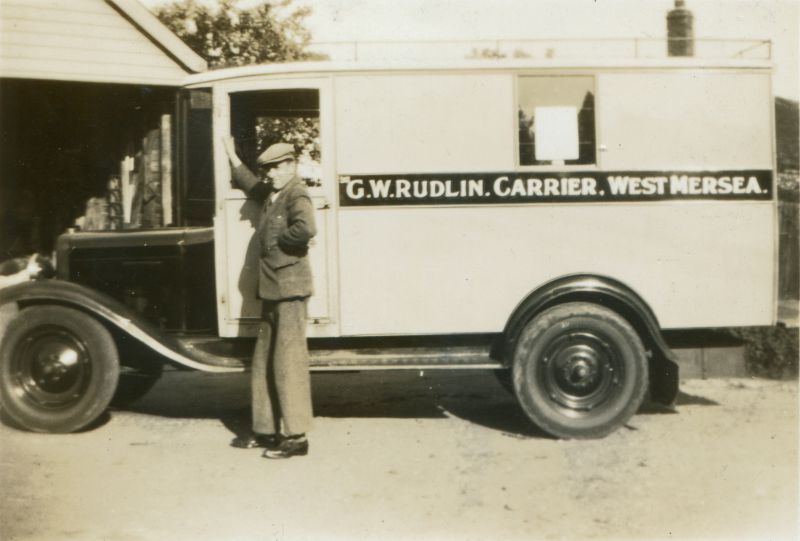  G.W. Rudlin Carrier, West Mersea. Driver is Arthur Death ex Digby's, who worked for George Rudlin. The Rudlin's first motorised carrier cart - the vehicle is a Chevrolet with bodywork by Maskell of Tollesbury. Outside the base in City Road where the cart was kept. 
Cat1 Transport - buses and carriers Cat2 Families-->Rudlin Cat3 [Display on front screen]
