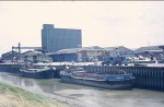  TRILBY (left) and BRANDRAM at Colchester Hythe in the 1970s.
 TRILBY was built Rochester in 1896 as a sailing barge. Official No. 106527. Like several of the barges on war service she was in a bad state at the end of the war and was rebuilt and enlarged. She was one of the last 
ex sailing barges to remain in trade.
 Sailing Barge Compendium records that TRILBY ceased trade in 1980; housebarge Weybridge, derelict 1995 at Watermans Park, Brentford.
 BRANDRAM was built 1915 as X Lighter X.67. In 1955 she was acquired by Bowker & King.

  <b>Comment 29 April 2012 by John Squires:</b>
 I can remember when I was a deckhand on the TRILBY, sleeping up the forehead end. The skipper was a man called Bob but I cannot remember his surname. We used to trade up and down the Thames taking Ammunition, Cement, and everything else round to Ipswich ( Paul's mills ) or to Harwich to unload the ammunition. We regularly used to moor up at Gravesend Reach and scull across to a pub called the Ship and Lobster, or if we were in Sheerness to a pub called the Rose. It was a hard life but a very good learning curve.
  <b>Comment by Mark Koenick 5 August 2012</b>
 I worked for Sully freight for about 5 years one of my skippers a man called Eric Goodall worked on the TRILBY having spent his entire working life with Sully Freight, who were a great company and treated there crews very fairly. We were paid a percentage of the value of the cargo, happy days, it all finished with the construction of the Euro Tunnel.
  <b>Comment added 7 November 2012:</b>
 Last skipper of the TRILBY was Bob Wells who lived on board for years. Barge is now a wreck in Brentford Creek with trees and bushes growing out of it.  SHP_STC_610
